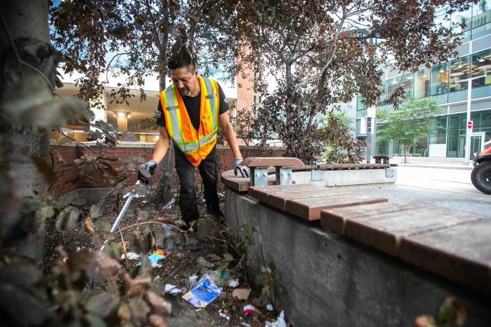 MIKAELA MACKENZIE / FREE PRESS
                                Downtown Winnipeg BIZ Enviro Team member Jeremy Roulette cleans trash from behind the bench at Carlton Street and Graham Avenue Wednesday.