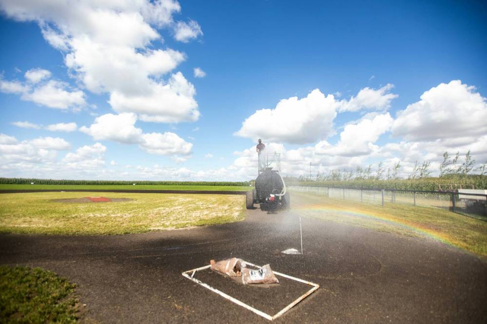 MIKAELA MACKENZIE / FREE PRESS
A rainbow forms over home plate as Jace Guilford waters the infield.