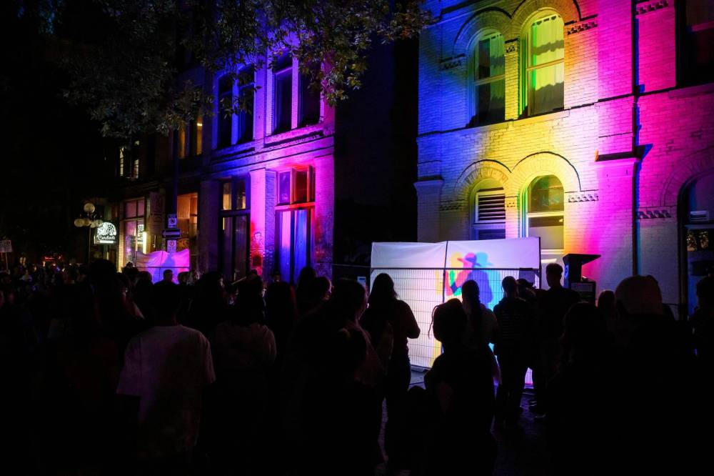 MIKE SUDOMA / FREE PRESS
Festivalgoers watch as musicians and dancers perform behind translucent white sheets, resulting in music and colour shining through to Albert Street in Winnipeg’s Exchange District.