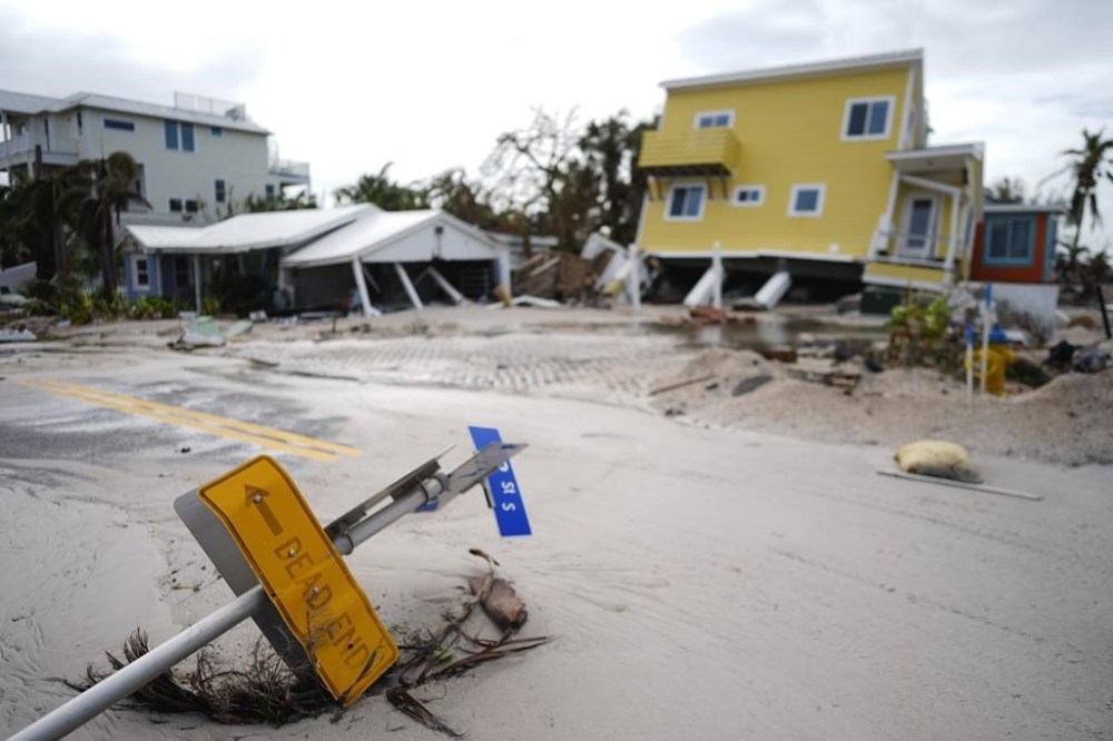 A house, top right, sits toppled off its stilts after the passage of Hurricane Milton, alongside an empty lot where a home was swept away by Hurricane Helene, in Bradenton Beach on Anna Maria Island, Fla., Thursday, Oct. 10, 2024. (AP Photo/Rebecca Blackwell)