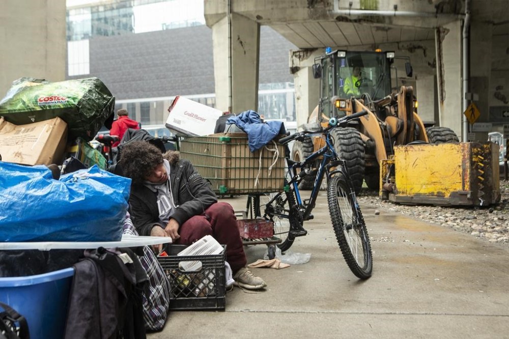 A person who experienced homelessness sits with their belongings as city workers move to clear an encampment on Toronto's Bay Street on May 15, 2020. THE CANADIAN PRESS/Chris Young