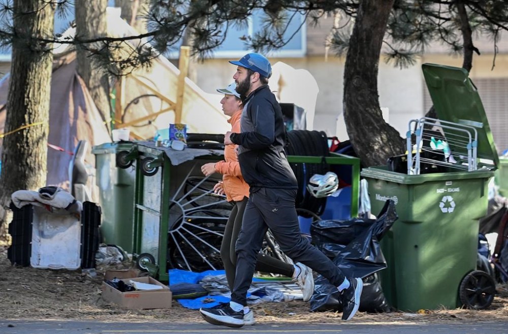 People jog by a homeless encampment on Notre-Dame Street in the east end of Montreal, Friday, Oct. 25, 2024. THE CANADIAN PRESS/Graham Hughes.