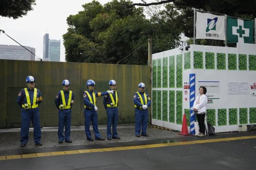 Mikiko Ishikawa, a university professor who protests against tree cutting stands right, as security guards stand in front of a gate of the Jingu Gaien park district of central Tokyo, Japan, where property developer Mitsui Fudosan begins cutting trees as part of the redevelopment of the area, Monday, Oct. 28, 2024. (AP Photo/Hiro Komae)