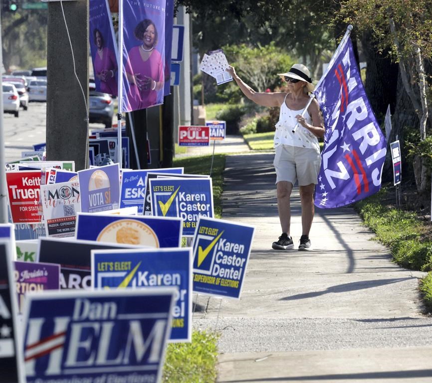 A campaign volunteer carries a Harris-Walz flag while waving to voters in line during early voting at the Orange County Supervisor of Elections precinct on Kaley Avenue in Orlando, Fla., Friday, Oct. 25, 2024. (Joe Burbank/Orlando Sentinel via AP)