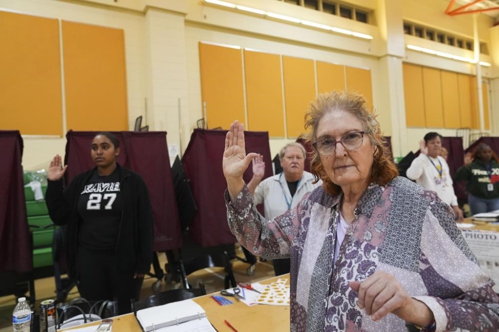 Holyn Robinson, a student at Xavier University, left, and Margie Robson, right, both first time precinct commissioners, take their oath along with fellow commissioners just before the opening of the polls, at the Hynes Charter School in New Orleans on Election Day, Tuesday, Nov. 5, 2024. (AP Photo/Gerald Herbert)