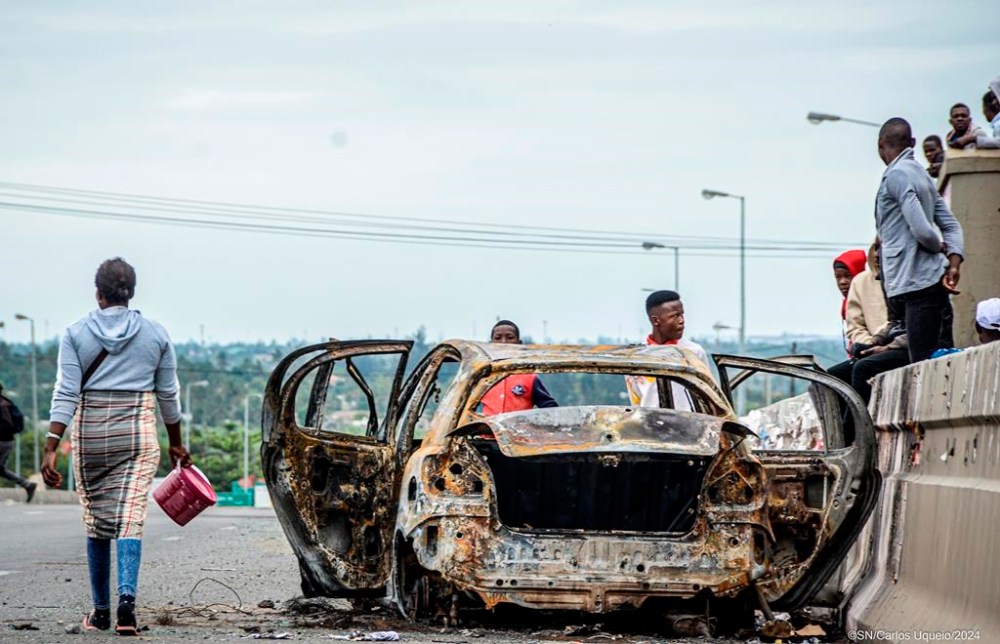 Pedestrians alongside burnt out vehicle Wednesday, Nov. 6, 2024 in Mozambique's capital Maputo, in protests that have engulfed the country after the opposition rejected the results of the country's polls which saw the Frelimo party extend its 58-year rule. (AP Photo/Carlos Uqueio)