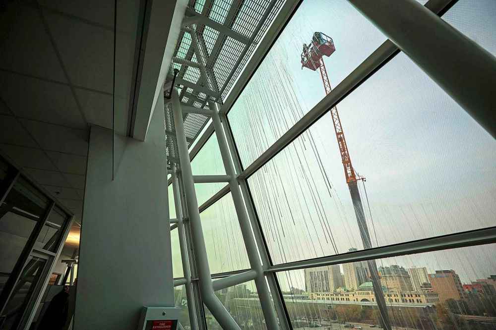 Jayden Vidal-Bircham helps direct a crane operator to maneuver close to the curved of glass of the CMHR building. (Ruth Bonneville / Free Press)