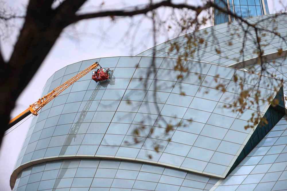 Jayden Vidal-Bircham continues washing the curved glass windows of the CMHR building on Friday. (Ruth Bonneville / Free Press)