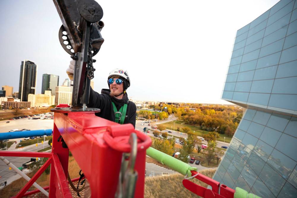 Jayden Vidal-Bircham washing the CMHR windows from bucket on a crane. (Ruth Bonneville / Free Press)