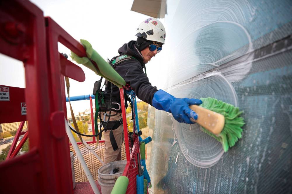 Jayden Vidal-Bircham, washing the CMHR windows from bucket on a crane. (Ruth Bonneville / Free Press)