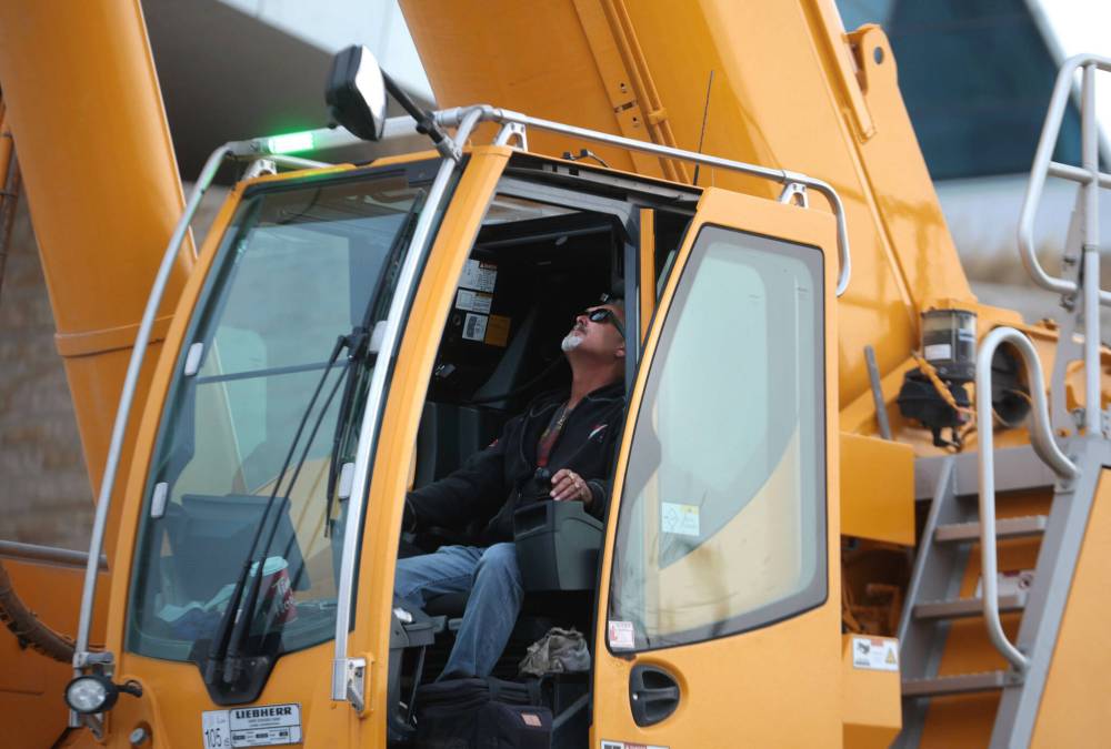 The crane operator maneuvers the window washers in the bucket up and down the walls of windows. (Ruth Bonneville / Free Press)