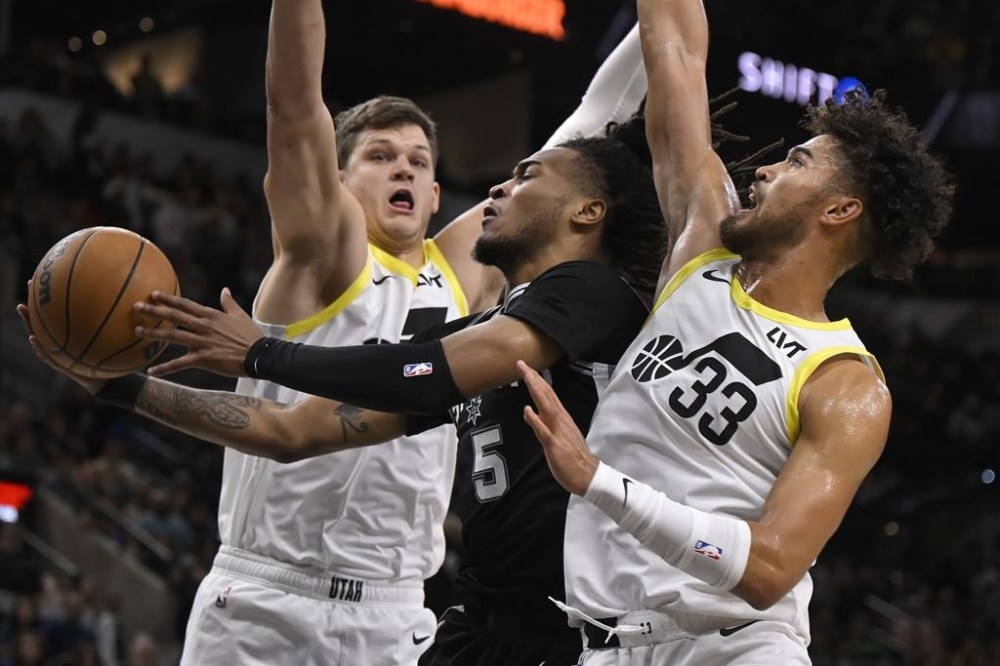 San Antonio Spurs' Stephon Castle (5) goes to the basket against Utah Jazz's Johnny Juzang (33) and Walker Kessler, left, during the first half of an NBA basketball game, Saturday, Nov. 9, 2024, in San Antonio. (AP Photo/Darren Abate)