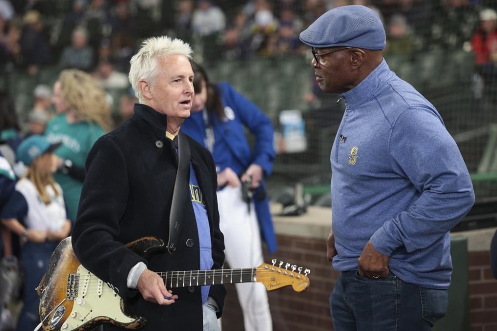 Pearl Jam guitarist Mike McCready, left, and Mariners broadcaster Dave Sims talk before McCready performs the national anthem at a baseball game between the Seattle Mariners and the Los Angeles Angels, Sunday, June 2, 2024, in Seattle. Sims is now going to be a play-by-play announcer for the New York Yankees. (AP Photo/Jason Redmond)