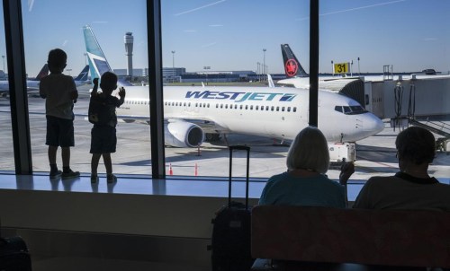 Young boys look out at Air Canada and WestJet planes at Calgary International Airport in Calgary, Alta., Wednesday, Aug. 31, 2022. Some travellers who checked baggage on certain WestJet flights between 2014 and 2019 may now claim their share of a class action settlement approved by British Columbia Supreme Court last month and valued at $12.5 million. THE CANADIAN PRESS/Jeff McIntosh