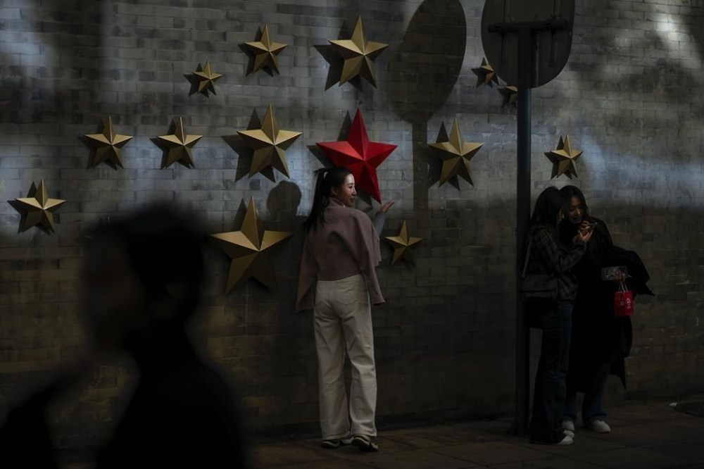 A beam of sunlight is cast on a woman as visitors take souvenir photos with the communist symbol of stars on display along a street in Beijing, Thursday, Nov. 21, 2024. (AP Photo/Andy Wong)