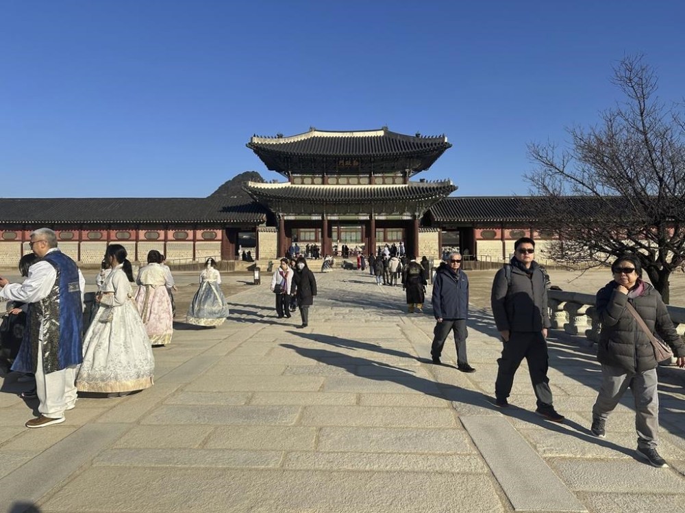 Tourists wearing traditional clothing rented from nearby shops pose for photos at at Gyeongbokgung Palace, in Seoul, Wednesday, Dec. 4, 2024. (AP Photo/ Jennifer McDermott)
