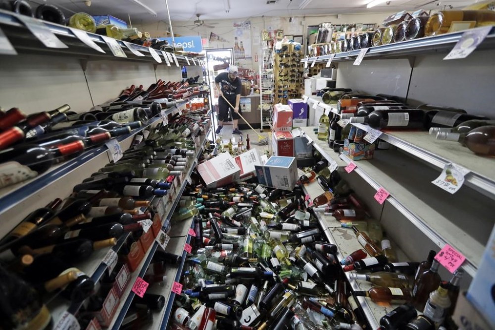FILE - Bottles of wine are strewn in the middle of an aisle as Victor Abdullatif, background center, mops inside of the Eastridge Market, his family's store, on July 6, 2019, in Ridgecrest, Calif., after an earthquake jolted the region from Sacramento to Las Vegas to Mexico. (AP Photo/Marcio Jose Sanchez, File)