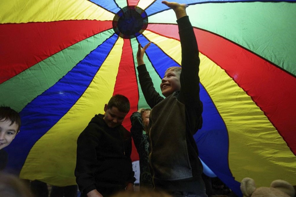 Children stand under a play parachute during an event organized by the local NGO Ukrainian Frontiers during celebration St. Nicholas Day in Izium, Ukraine, Dec. 6, 2024. (AP Photo/Evgeniy Maloletka)