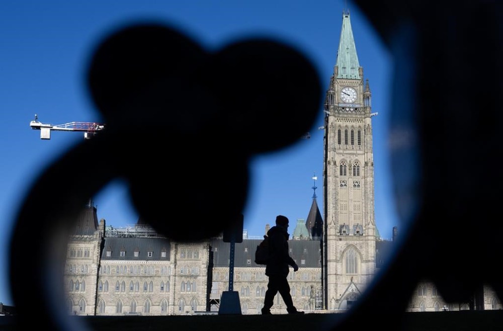 A man is silhouetted as buildings cast their shadows in front of the Peace tower on Parliament Hill, in Ottawa, Wednesday, Nov. 27, 2024. THE CANADIAN PRESS/Adrian Wyld