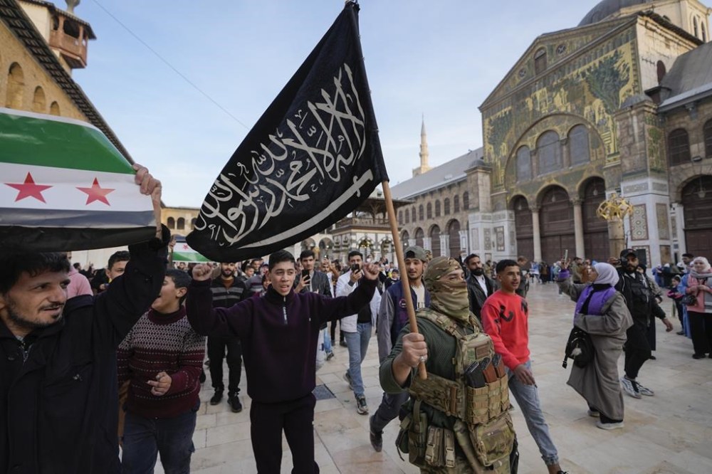 A masked opposition fighter carries a flag of Hayat Tahrir al-Sham (HTS) in the courtyard of the Umayyad Mosque in the old walled city of Damascus, Syria, on Tuesday, Dec. 10, 2024. HTS is the largest rebel faction within the opposition that toppled Bashar Assad's regime last Sunday. (AP Photo/Hussein Malla)