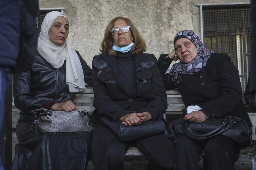 Three women wait outside the morgue to identify missing relatives or friends at the Al-Mujtahidh hospital in Damascus, Syria, Tuesday, Dec. 10, 2024. (AP Photo/Ghaith Alsayed)