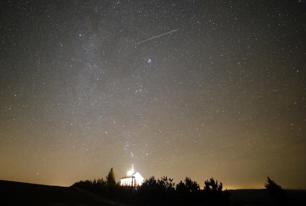 FILE - A meteor streaks across the sky during the annual Geminids meteor shower over an Orthodox church on the local cemetery near the village of Zagorie, Belarus, late, Dec. 13, 2017. (AP Photo/Sergei Grits, File)
