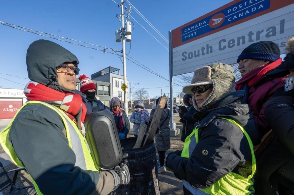 Striking Canada Post employees listen on a speaker to the news that Federal Labour Minister Steven MacKinnon is asking the Canada Industrial Relations Board to send the 50,000 employees back to work, in Toronto on Friday, Dec. 13, 2024. THE CANADIAN PRESS/Frank Gunn