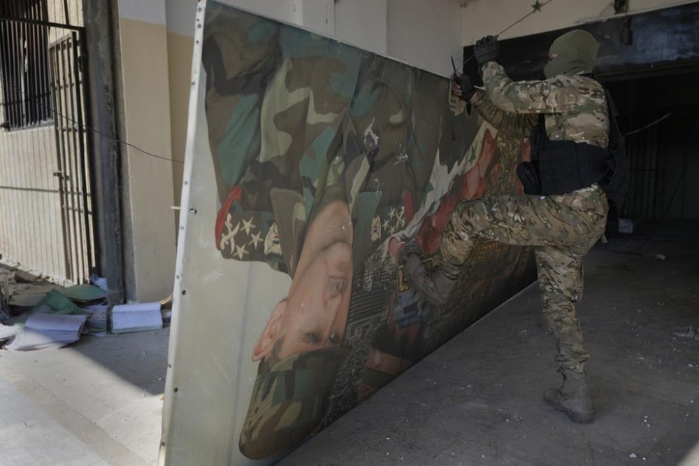 A Syrian fighter from rebel group, removes a poster at the entrance to the notorious security detention centre called Palestine Branch, which shows the ouster Syrian President Bashar Assad in Damascus, Syria, Saturday, Dec. 14, 2024. (AP Photo/Hussein Malla)