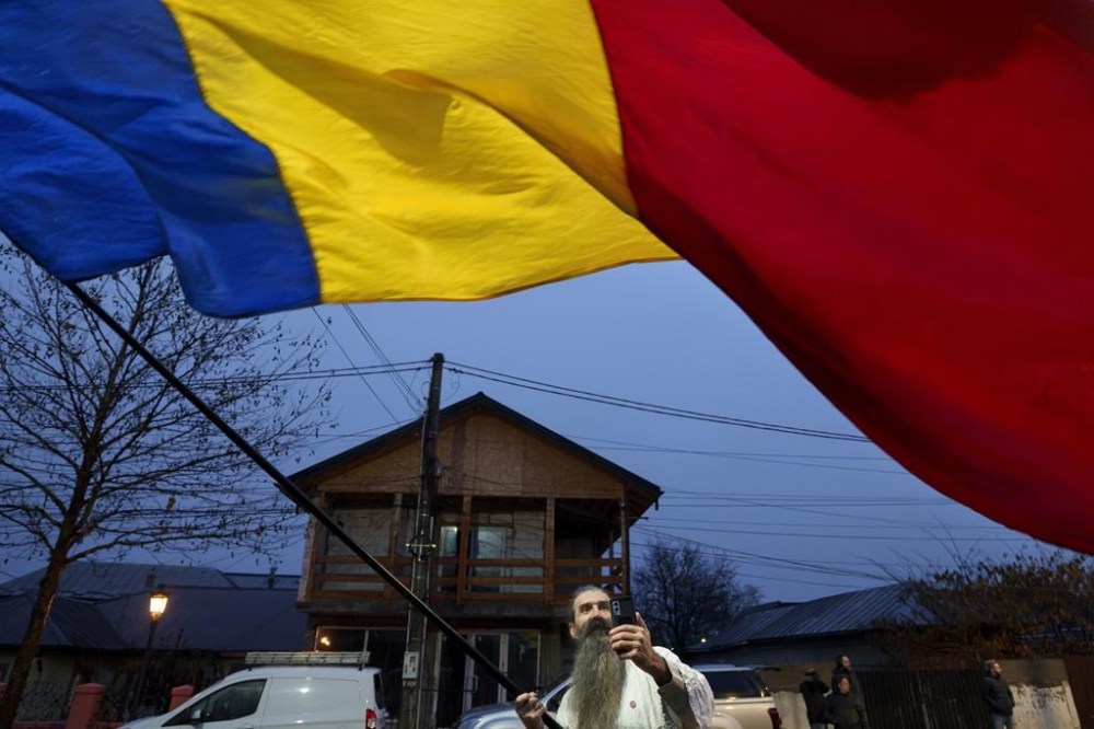 A man waves the Romanian flag outside the closed voting station where Calin Georgescu, an independent candidate for president who won the first round of presidential elections, was supposed to vote, after Romania's Constitutional Court annulled the first round of presidential elections, in Mogosoaia, Romania, Sunday, Dec. 8, 2024. (AP Photo/Andreea Alexandru)