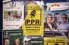Posters of various political parties, one showing a man pointing a thermometer at a statue of Ellie Wiesel and reading 