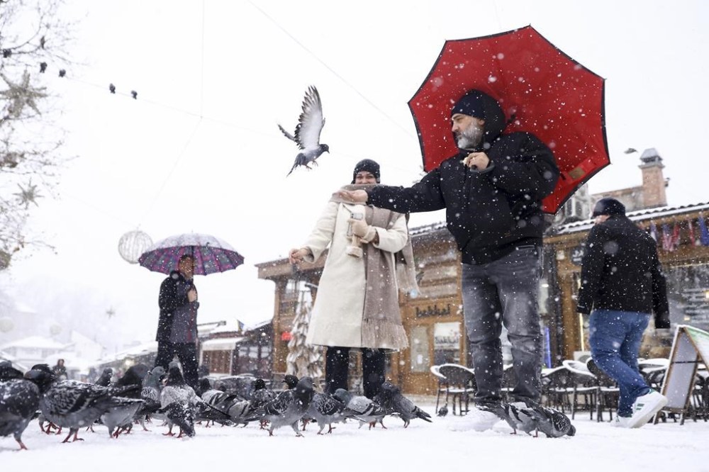 Tourists feed pigeons during heavy snowfall in downtown Sarajevo, Bosnia, Monday, Dec. 23, 2024. (AP Photo/Armin Durgut)