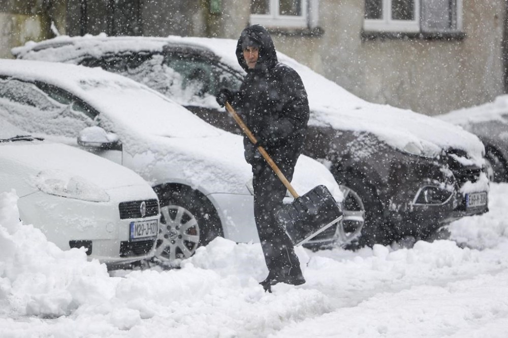 A man shovels snow from the street during heavy snowfall in Bihac, Bosnia, Monday, Dec. 23, 2024. (AP Photo/Edvin Zulic)