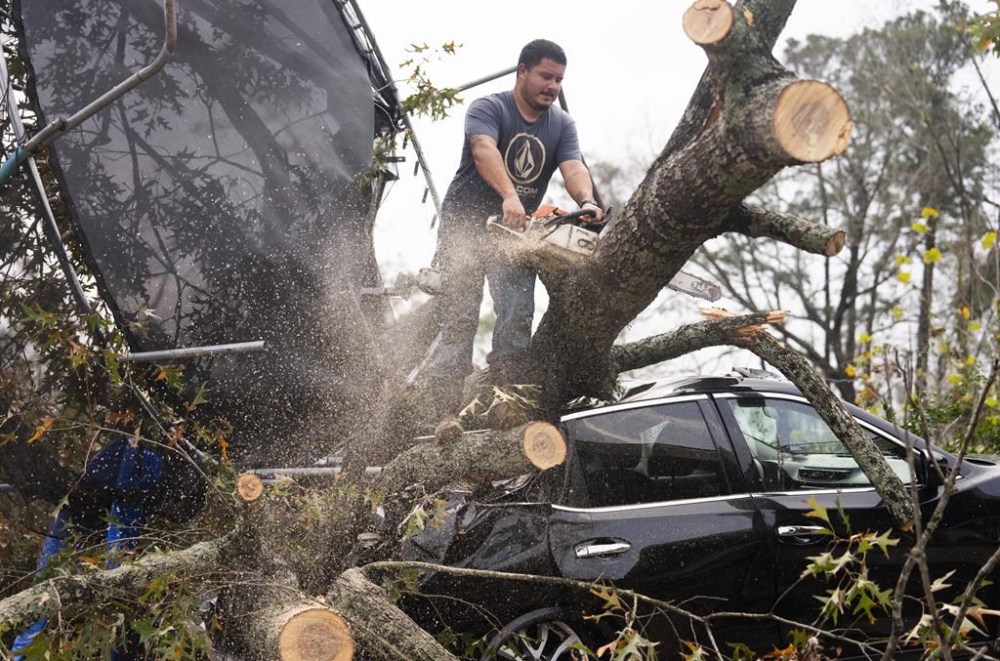 Saul Rodriguez uses a chain saw to remove debris atop a car from a woman's home after strong thunderstorms pass through the Greater Houston region, Saturday, Dec. 28, 2024, in Porter Heights. (Jason Fochtman/Houston Chronicle via AP)