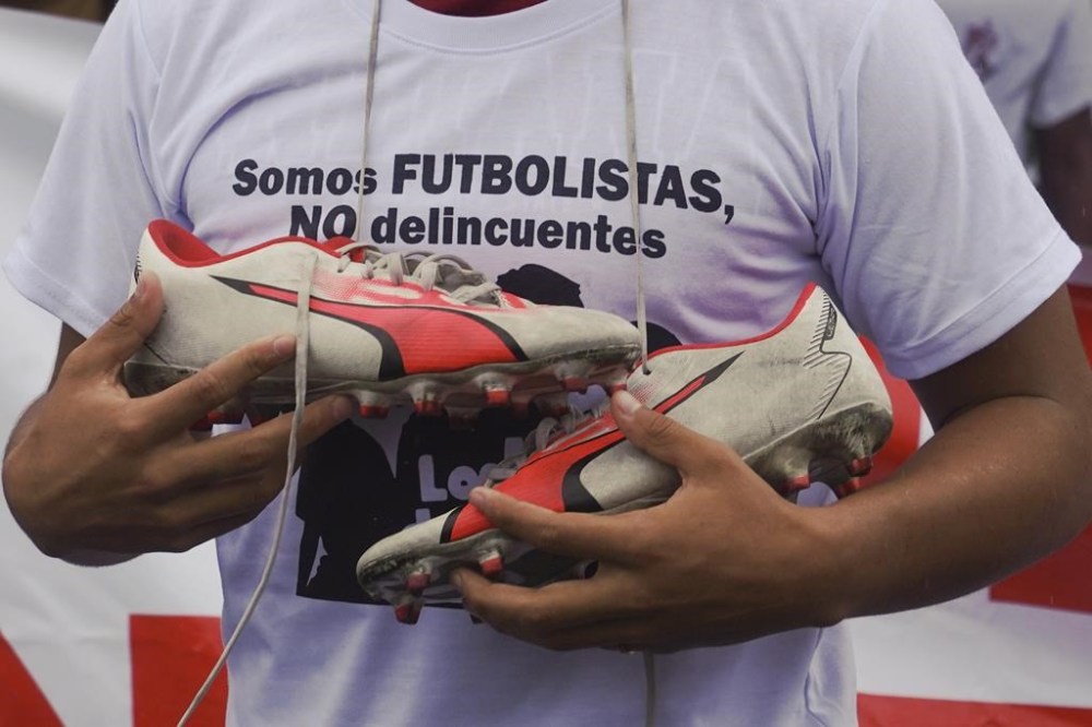 A protester holds soccer cleats and wears a shirt that reads in Spanish