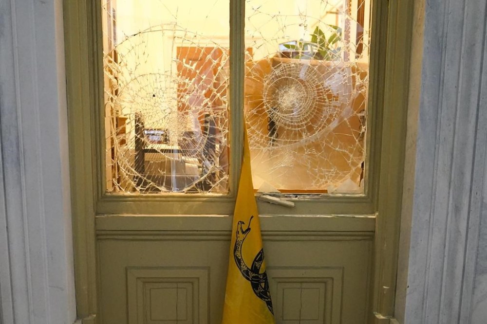 A flag hangs between broken windows after supporters of then-President Donald Trump tried to break through police barriers outside the U.S. Capitol, Jan 6, 2021. (AP Photo/John Minchillo, File)