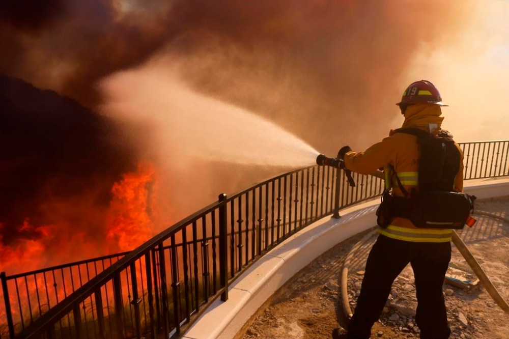 A firefighter makes a stand in front of the advancing Palisades Fire in the Pacific Palisades neighborhood of Los Angeles, Tuesday, Jan. 7, 2025. (AP Photo/Etienne Laurent)