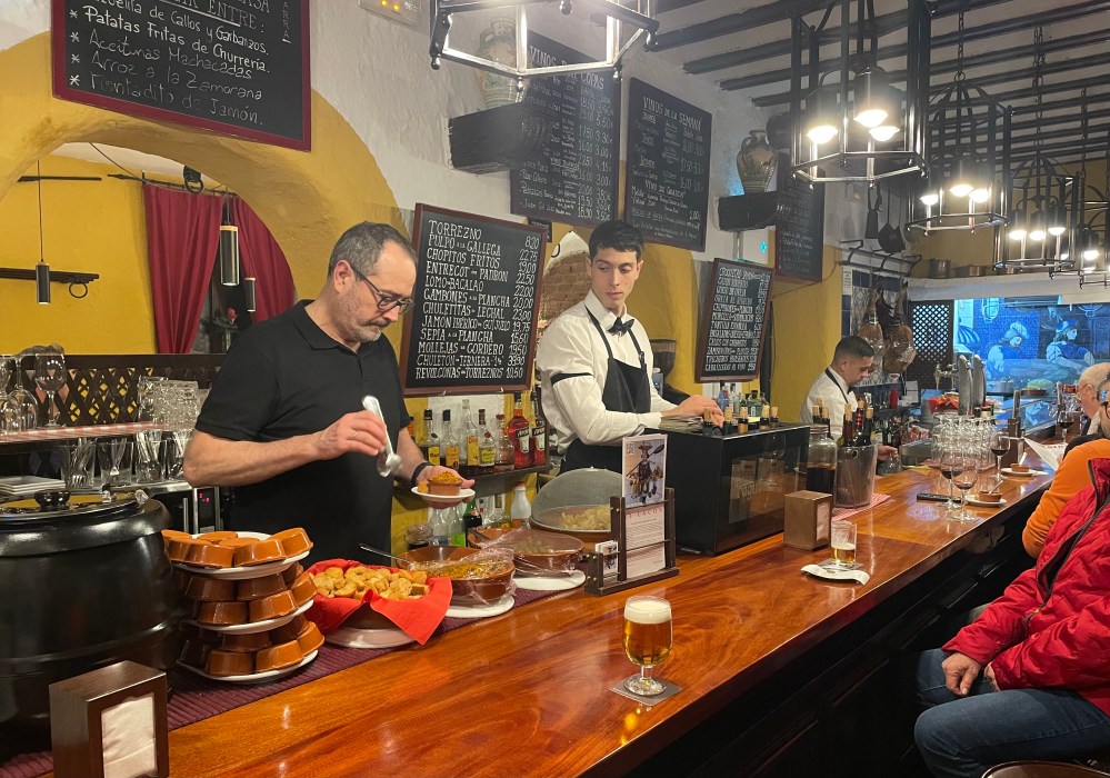 photos by Steve MacNaull
The bar at El Lacon: eat your tapas and drink your beverages at the bar, ‘where the best gossip is,’ according to tour guide and chef Arantxa Lamas (inset).