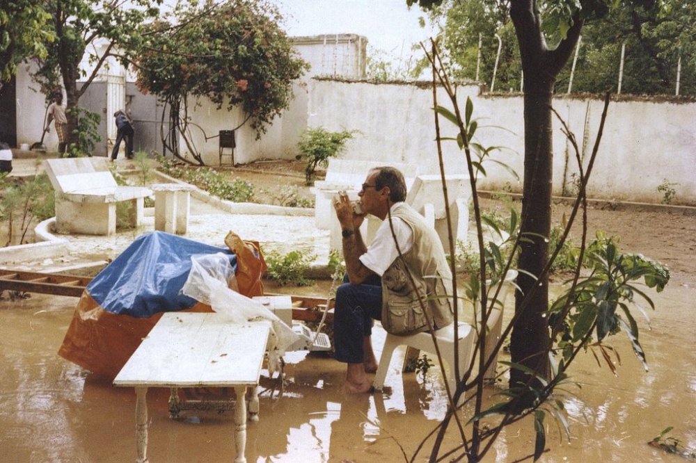 AP journalist Reid G. Miller speaks on a phone while sitting barefoot in the mud in a U.N. compound in November 1994, in Mogadishu, Somalia. Miller, a longtime AP journalist in many places around the world, died Thursday, Feb. 6, 2025. (AP Photo/Tina Susman)