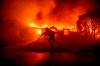 A firefighter battles the Palisades Fire as it burns a structure in the Pacific Palisades neighborhood of Los Angeles, Tuesday, Jan. 7, 2025. (AP Photo/Ethan Swope)