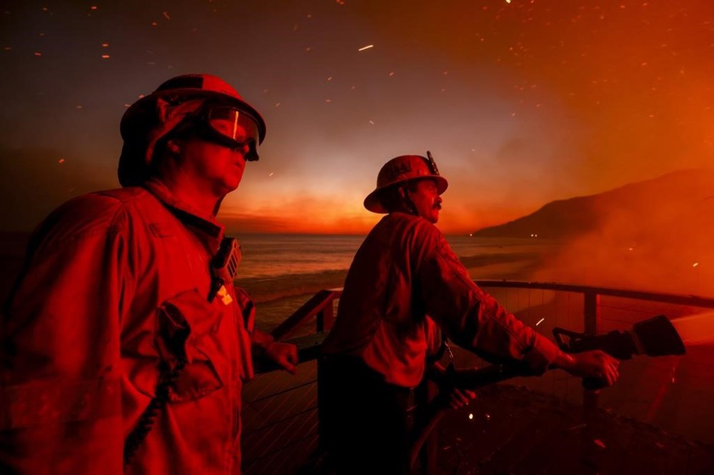 Firefighters work from a deck as the Palisades Fire burns a beachfront property Wednesday, Jan. 8, 2025 in Malibu, Calif. (AP Photo/Etienne Laurent)