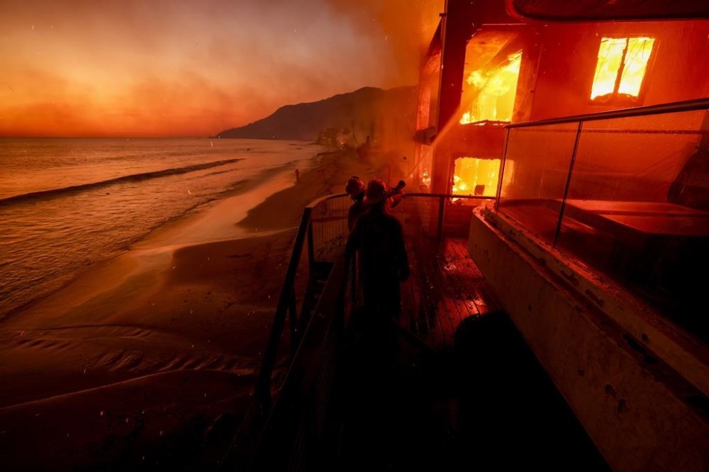 Firefighters work from a deck as the Palisades Fire burns a beachfront property Wednesday, Jan. 8, 2025 in Malibu, Calif. (AP Photo/Etienne Laurent)