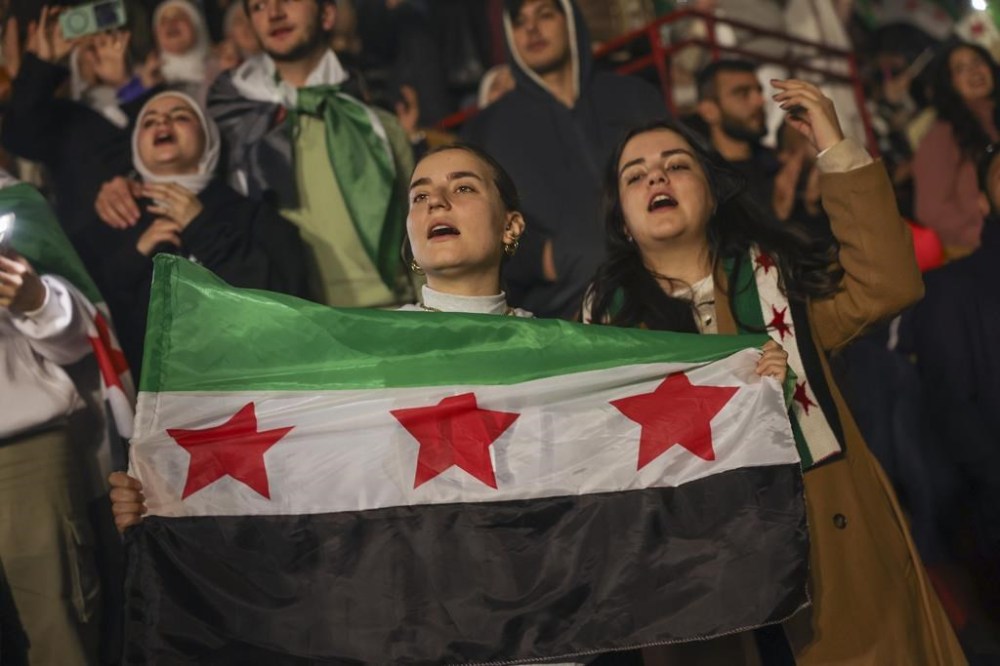 Syrians sing and hold a post-Assad flag during a concert by the recently returned