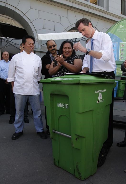 FILE - San Francisco Mayor Gavin Newsom, right, signs a mandatory recycling and composting ordinance on top of a compostable collection bin at the Ferry Building in San Francisco, Tuesday, June 23, 2009. Looking on at left is executive chef Charles Phan of The Slanted Door restaurant. (AP Photo/Eric Risberg, file)