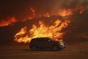A vehicle rides past a hillside engulfed in flames caused by the Hughes Fire in Castaic, Calf., Wednesday, Jan. 22, 2025. (AP Photo/Ethan Swope)