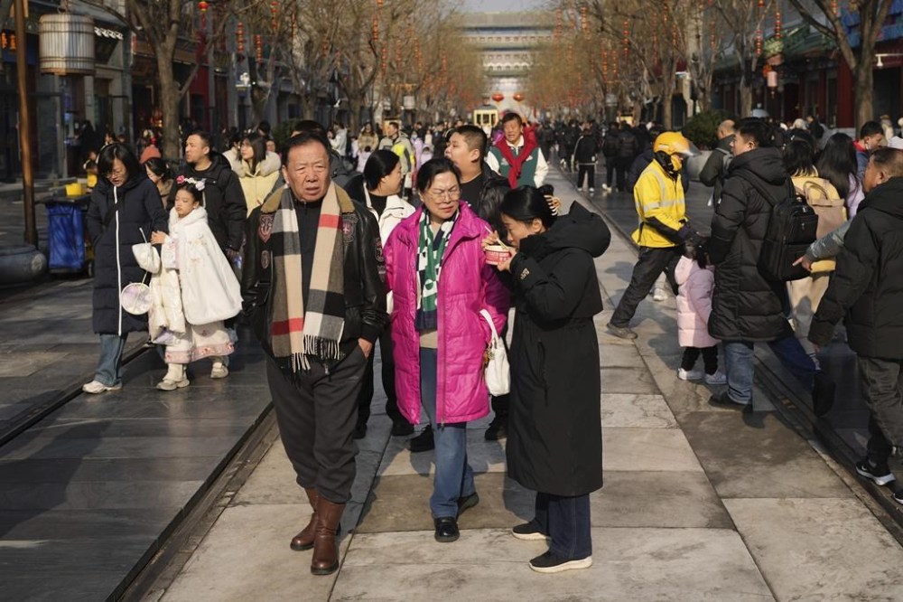 A woman eats noodles along a crowded street at a commercial area in Beijing on Thursday Jan. 23, 2025. (AP Photo/Aaron Favila)