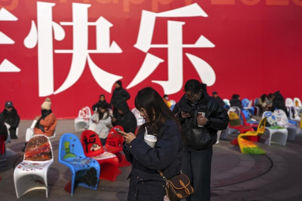 Women walk by people taking a rest on the chairs near a huge display board carrying the words, meaning