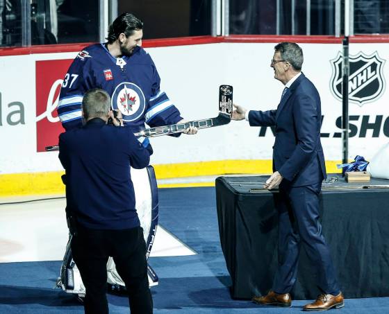 Winnipeg Jets Executive Chairman Mark Chipman (right) presents Connor Hellebuyck with special sticks to celebrate his 300th win, 500 regular season games and 40th shutout prior to the game Friday. (John Woods / The Canadian Press)