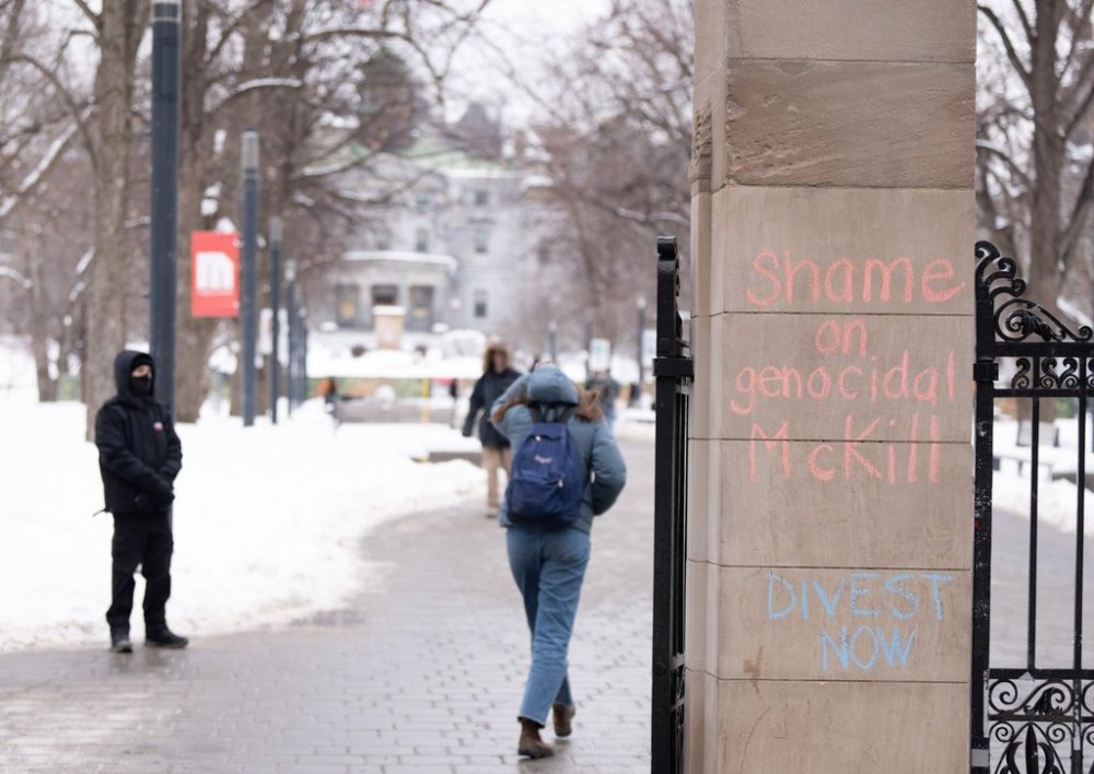 Students walk past vandalism sprayed on the Roddick Gates of McGill University in Montreal on Thursday, Feb. 6, 2025. Police are investigating after they allege a group smashed windows and graffitied the message