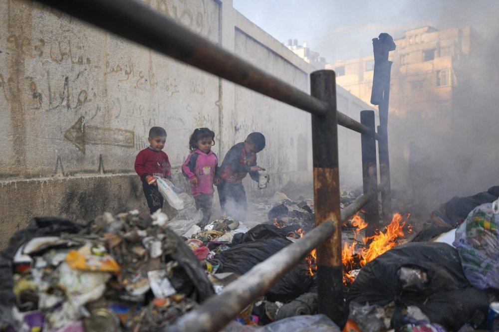 From left to right, Awad, Salma, and Mahmoud play by throwing paper onto a burning pile of garbage in the streets, as there is no refuse collection and people are disposing of their rubbish in the open, in Gaza City, Tuesday, Feb.4, 2025. (AP Photo/Abdel Kareem Hana)