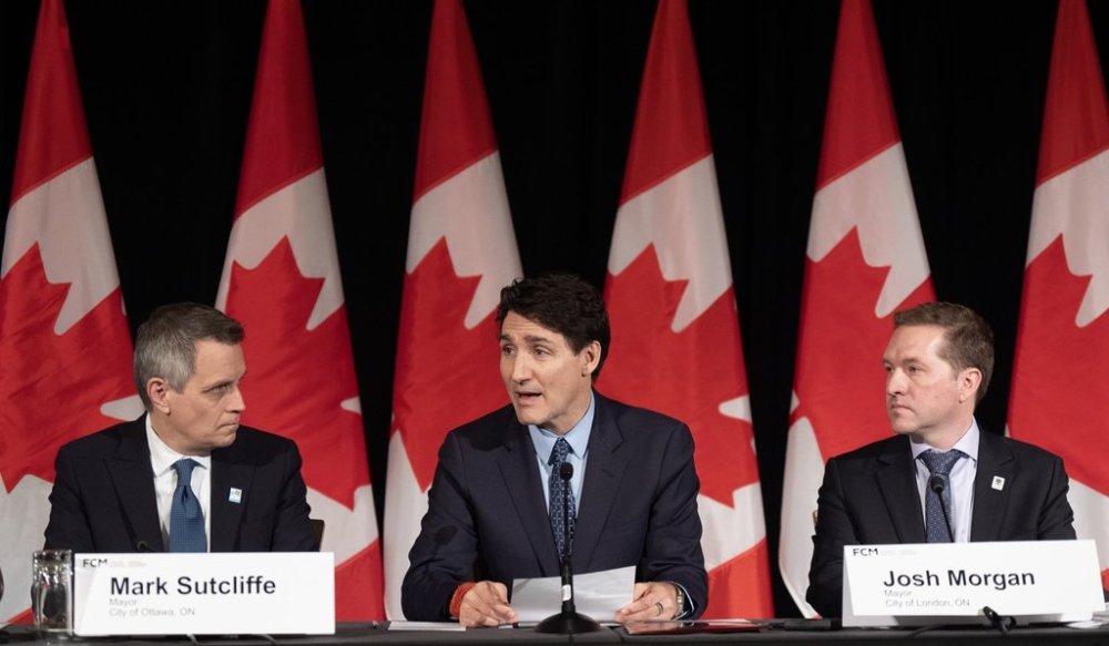 Ottawa Mayor Mark Sutcliffe, left, and London Mayor Josh Morgan, right, look on as Prime Minister Justin Trudeau speaks to the Federation of Canadian Municipalities’ Big City Mayors Caucus meeting, Thursday, Feb. 6, 2025 in Ottawa. THE CANADIAN PRESS/Adrian Wyld